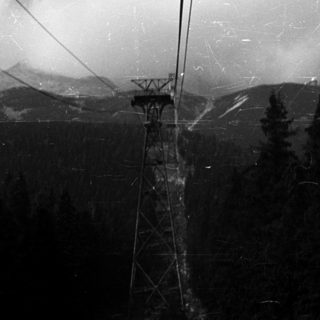 Monochrome image of a ski lift over a forest and mountains.