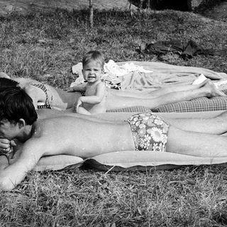 People sunbathing on grass, with a baby nearby.