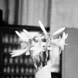 Woman in lab coat smiles while holding flowers.