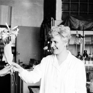 Woman in lab coat smiles while holding flowers.