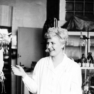 Woman in lab coat displays a plant specimen.