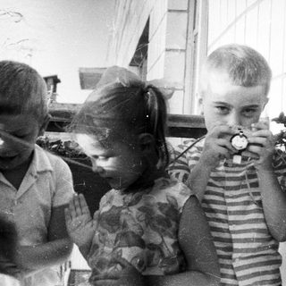 Three children looking at something with a vintage device.