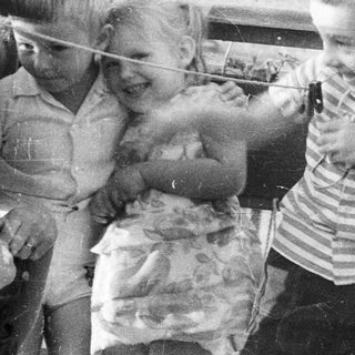 Three children play with a string on an outdoor balcony.