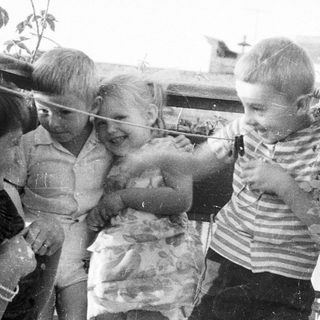 Three children play with a string on an outdoor balcony.
