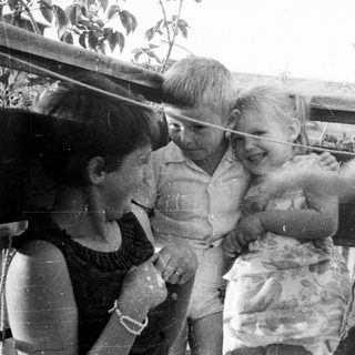 Three children play with a string on an outdoor balcony.