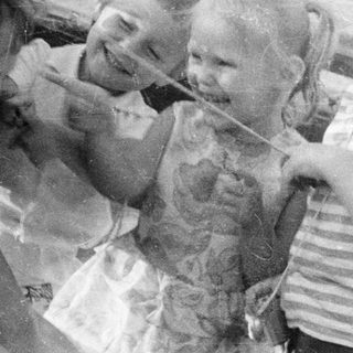Black and white photo depicts three children and an adult outdoors.