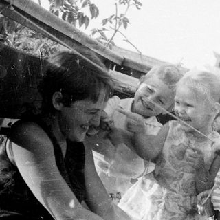 Black and white photo depicts three children and an adult outdoors.
