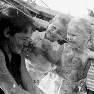 Black and white photo depicts three children and an adult outdoors.