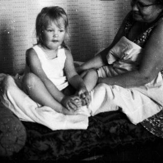 Child and adult sitting on a bed together.