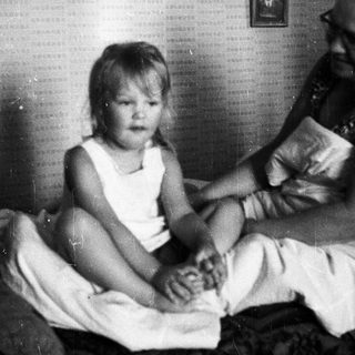 Child and adult sitting on a bed together.