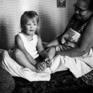 Child and adult sitting on a bed together.