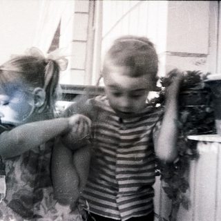 Here's a brief summary of the image: Three children appear in a blurry, vintage outdoor scene.