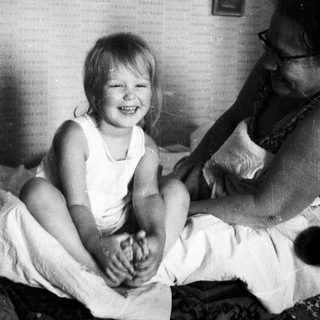 A smiling child sits on a bed with an adult.