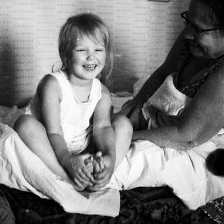 A smiling child sits on a bed with an adult.