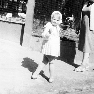 Child stands near animal enclosure with a woman.