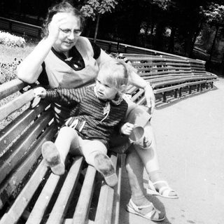 Woman and child sit on a park bench together.