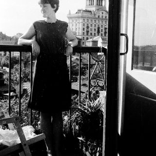 Woman stands on balcony overlooking a building and city.