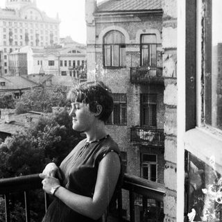 Woman stands on balcony, overlooking a city skyline.