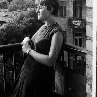 Woman stands on balcony, overlooking a city skyline.