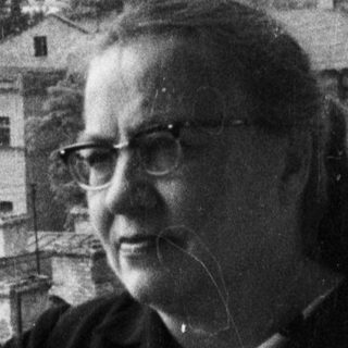 Woman stands on balcony overlooking a city and large building.