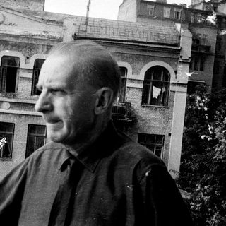 Man stands near building, looking off to the side.