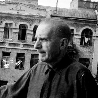 Man stands near building, looking off to the side.
