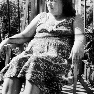 Woman in a dress sits on a porch rocker.