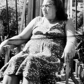 Woman in a dress sits on a porch rocker.