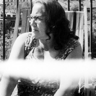 Woman sits outdoors, overlooking a building with a tower.
