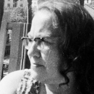 Woman sits outdoors, overlooking a building with a tower.