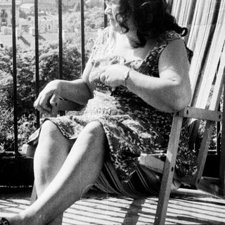 Here's a brief summary of the image: Woman relaxes in a wooden chair on a balcony.