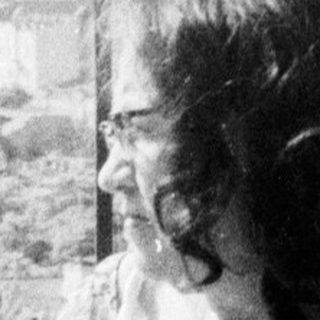 Here's a brief summary of the image: Woman relaxes in a wooden chair on a balcony.
