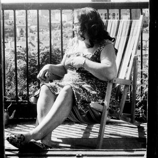 Here's a brief summary of the image: Woman relaxes in a wooden chair on a balcony.