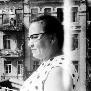 Woman standing on a balcony with a building behind.