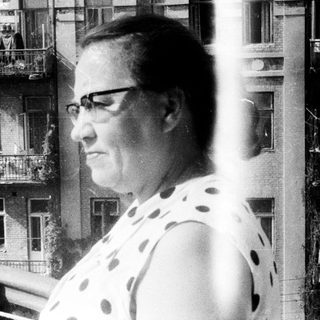 Woman standing on a balcony with a building behind.