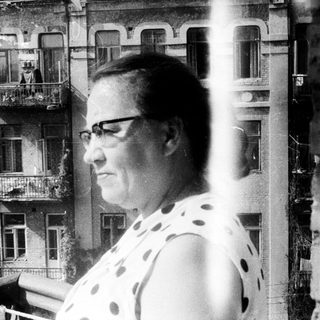 Woman standing on a balcony with a building behind.
