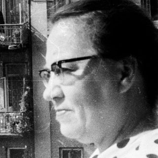 Woman standing on a balcony with a building behind.