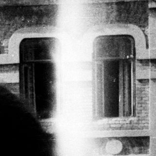 Woman standing on a balcony with a building behind.
