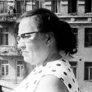 Woman stands on a balcony, overlooking a building.