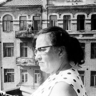 Woman stands on a balcony, overlooking a building.