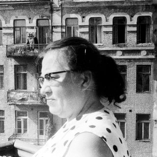 Woman stands on a balcony, overlooking a building.