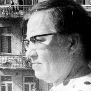 Woman stands on a balcony, overlooking a building.