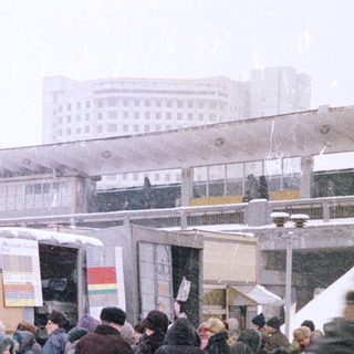 Crowded market scene with snow falling and a train station.