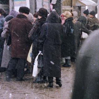 Crowded market scene with snow falling and a train station.
