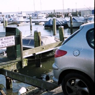 Marina with numerous boats docked, a car, and a sign.