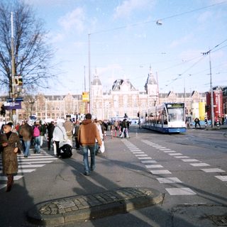 People crossing street near a train station building.
