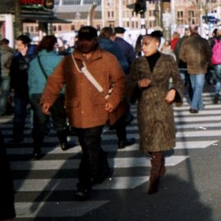 People crossing street near a train station building.