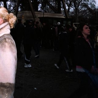Woman stands near the Eiffel Tower in a public space.