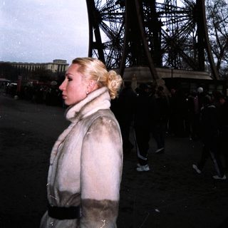 Woman stands near the Eiffel Tower in a public space.