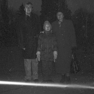 Here's a brief summary of the image: Two people stand on a ledge in low light.